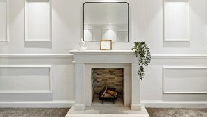 A white fireplace with a framed mirror above it, a mantel with a small plant, and a log fire inside.