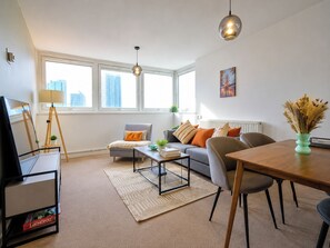 A modern living room with a sofa, coffee table, dining table, and a TV on a stand. - Stylish 2 Bed Flat Near Old Street (Greater London)
