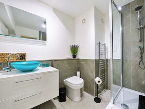 A modern bathroom with a large mirror, a blue vessel sink, a toilet, a shower with a glass enclosure, and a towel rack. - Stylish 2 Bed Flat Near Old Street (Greater London)
