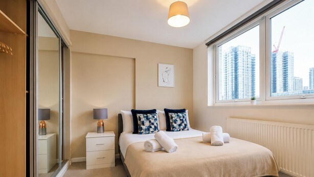 Una habitación de hotel moderna con cama, mesitas de noche, un ventanal con vistas a la ciudad y un radiador.