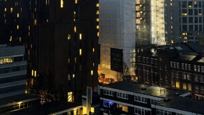 Un paisaje urbano con modernos edificios altos, incluyendo un edificio rectangular destacado con una grúa en la parte superior.