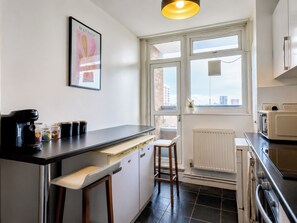 A kitchen with a coffee machine, jars, a window, and a radiator. - Stylish 2 Bed Flat Near Old Street (Greater London)