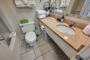 Ein Badezimmer mit Toilette, Waschbecken und Spiegel. Auf der Ablage liegen Handtücher und Toilettenartikel.
