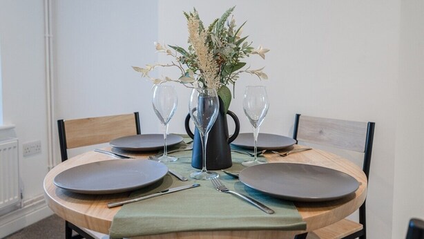 A round dining table with four plates, two wine glasses, and a vase with flowers.