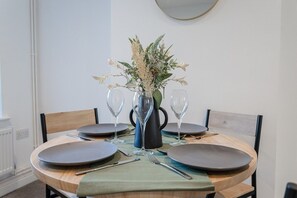 A round dining table with four plates, two wine glasses, and a vase with flowers. - Bright & Cosy 3 Bed Home I Parking I Sleeps 6 (Suffolk)