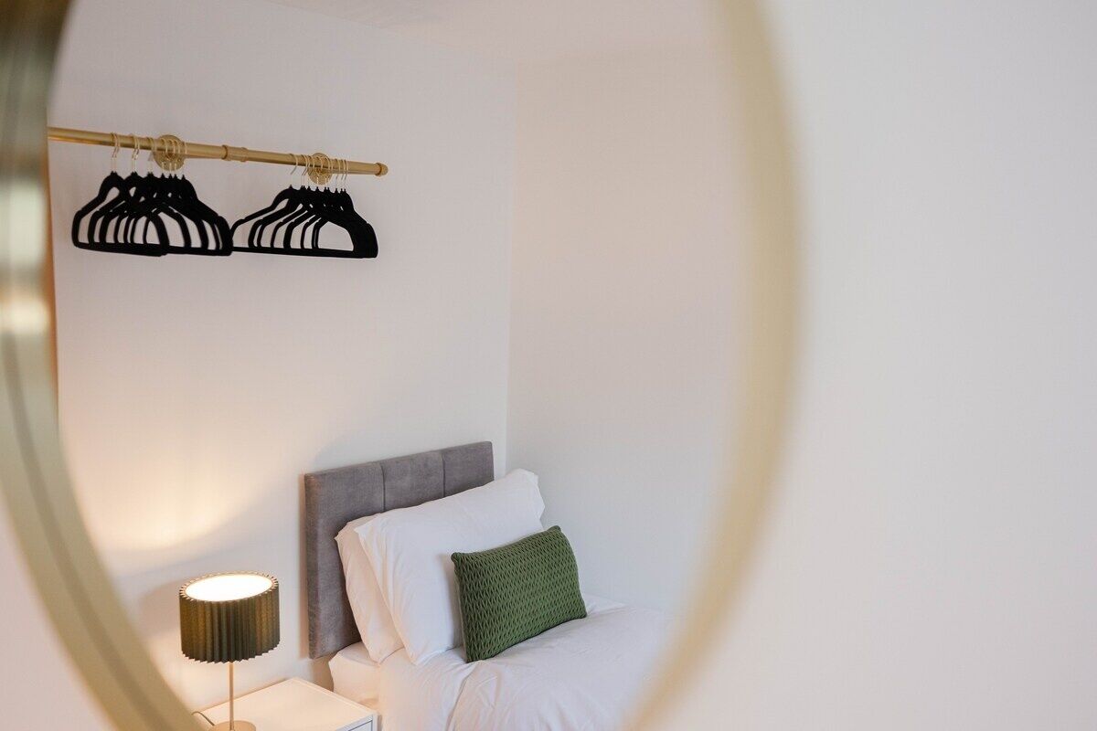 A hotel room with a bed, a nightstand, a lamp, and a clothing rack with hangers.