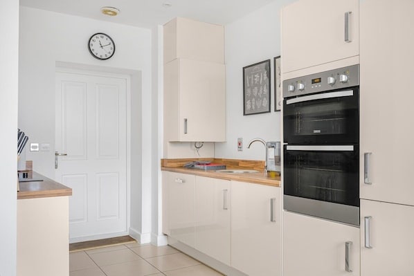 Una cocina moderna con armarios blancos, horno doble y encimera de madera.