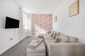 Una sala de estar moderna con un sofá color crema, un televisor de pantalla plana montado en la pared y un papel tapiz con estampado floral.