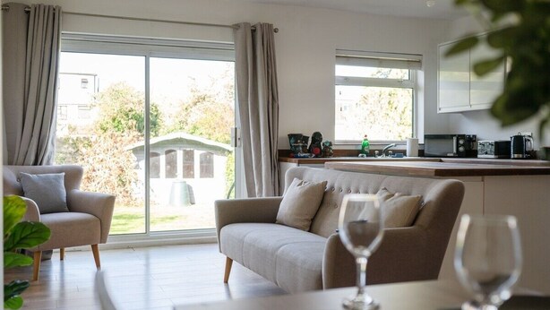 A modern living room with a sofa, a dining table, and a kitchen area with a microwave and coffee maker.
