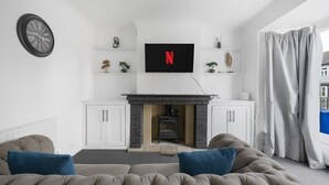 Un salon avec une cheminée, un téléviseur fixé au-dessus, et un canapé avec des coussins.
