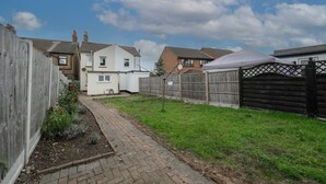 Un jardin à l’arrière d’une maison, avec un chemin dallé, une clôture en bois et une maison blanche.
