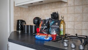 Un plan de travail de cuisine sur lequel on trouve divers objets, notamment une bouilloire, une bouteille d’huile d’olive et des paquets de collations.