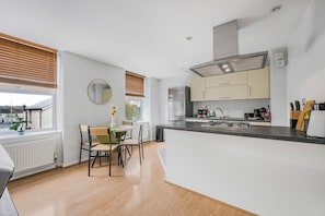 A modern kitchen with a central island, a dining area with a table and chairs, and a view through the window. - Chelmsford City Flat I Secure Parking I Sleeps 4 (Essex)