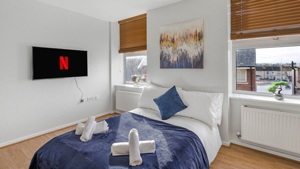 Une chambre à coucher moderne avec un lit, un téléviseur fixé au mur, une fenêtre avec des stores et un tableau.