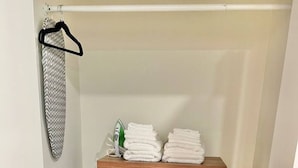A wooden dresser with three drawers, a hanging garment rack, and a stack of folded towels.