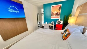 A hotel room with a large bed, a desk with a chair, a TV displaying the Disney+ logo, a poster on the wall, and a red suitcase. - Boutique Hotel - King Room - Far Out Motel (Starkville)