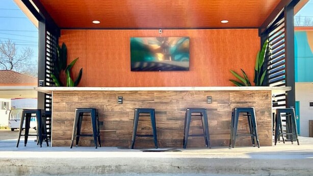 A modern bar area with a wooden ceiling, a large abstract painting, and several stools. - Boutique Hotel - King Room - Far Out Motel (Starkville)