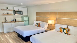 Habitación de hotel con dos camas, kitchenette y cabecera de madera.
