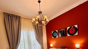 A hotel room with a bed, a chandelier, a nightstand, and a window with curtains.