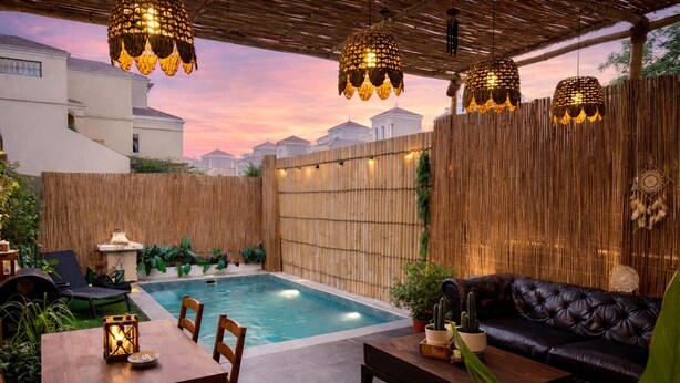 A backyard with a swimming pool, a dining table, a sofa, and hanging lights.