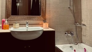 A bathroom with a large mirror, a sink, a shower, and a bathtub with rose petals.