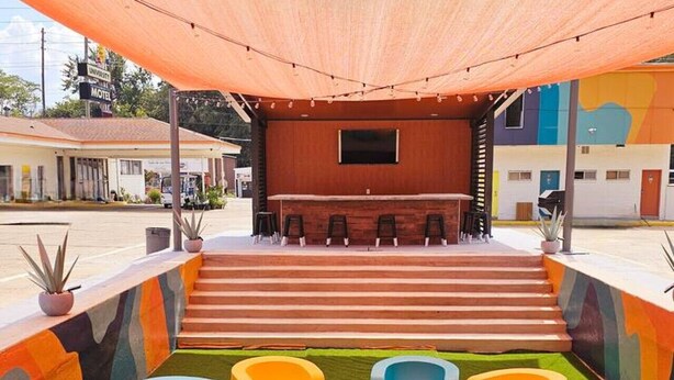 A covered outdoor seating area with colorful, modern chairs and a wooden bench.