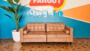 A room with a brown sofa, a potted plant, and a wall with a 'FAROUT HOTEL' sign.