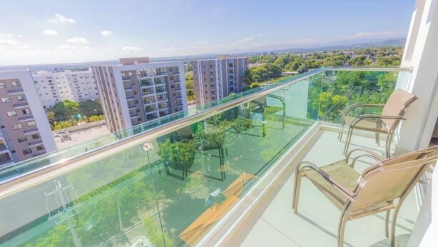 Een balkon met glazen hekwerk met uitzicht op een stadsgezicht, met moderne gebouwen en groen.