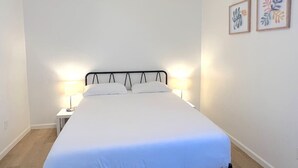 Un lit bien fait, avec une literie blanche, deux lampes de chevet et deux œuvres d’art encadrées accrochées au mur.