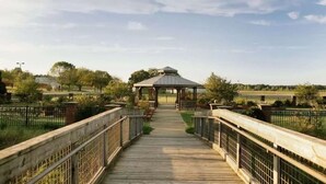 A wooden boardwalk leading to a gazebo in a park with fenced areas and trees.