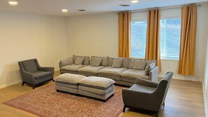 A living room with a sectional sofa, two armchairs, a small ottoman, and a patterned rug.