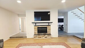 A modern living room with a stone fireplace, a flat-screen TV mounted above it, and a staircase leading to another level.
