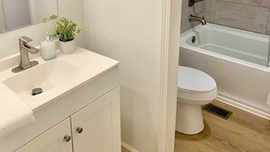 Une salle de bain avec un meuble-lavabo blanc, un évier, un miroir, des toilettes et un espace douche.