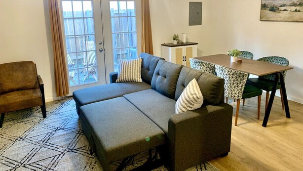 Un salon comprenant un canapé, une table à manger et des chaises. Il y a une fenêtre avec des rideaux, un ventilateur de plafond et un tableau accroché au mur.