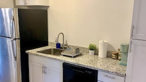 Une cuisine compacte avec des meubles blancs, un réfrigérateur en acier inoxydable, un lave-vaisselle et un plan de travail en granit.