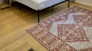Une chambre à coucher avec un lit, une table de chevet avec une lampe, un ventilateur de plafond, une fenêtre avec des rideaux et un tapis à motifs.