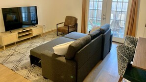 Un salon moderne avec un canapé, un fauteuil, un téléviseur et un balcon agrémenté de rideaux.