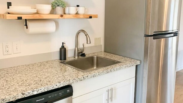 A modern kitchen with white cabinets, a stainless steel refrigerator, granite countertop, and a dishwasher. - Central MSU Explorer`s Nest 2BR (Starkville)
