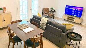 A living room with a sofa, a dining table with chairs, a TV, and a ceiling fan. - Central MSU Explorer`s Nest 2BR (Starkville)