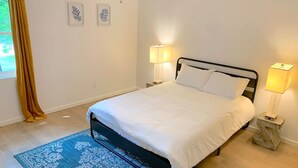 A bedroom with a bed, two bedside lamps, a blue patterned rug, and a window with curtains. - Central MSU Explorer`s Nest 2BR (Starkville)