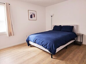A bedroom with a bed, a bedside table, a floor lamp, and a framed picture on the wall.