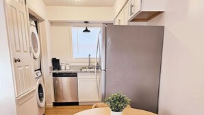 A compact kitchen with a round wooden table, a built-in dishwasher, and a refrigerator. - Cozy 2-Bedroom Haven: Sleeps 5! (Starkville)