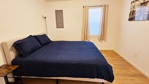 A bedroom with a bed, a nightstand, a window with curtains, and a wall-mounted light fixture. - Cozy 2-Bedroom Haven: Sleeps 5! (Starkville)
