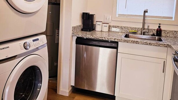 A compact kitchen with a dishwasher, a sink, and a window with blinds. - Cozy 2-Bedroom Haven: Sleeps 5! (Starkville)