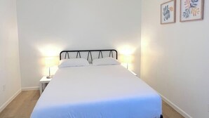 Un lit bien fait, avec du linge de lit blanc, dans une chambre sobre agrémentée de deux lampes de chevet.