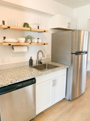 Een moderne keuken met witte kasten, een roestvrijstalen koelkast, een granieten aanrecht en een vaatwasser.
