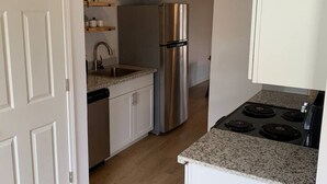 A modern kitchen with white cabinetry, a stainless steel refrigerator, a built-in oven, and a granite countertop. - MSU Sweet Spot: Cozy 2BR w/Patio (Starkville)