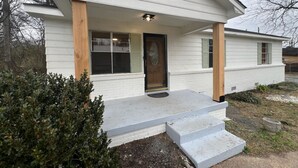 Une maison de plain-pied avec un porche à l’avant, une porte en bois et un petit jardin devant.