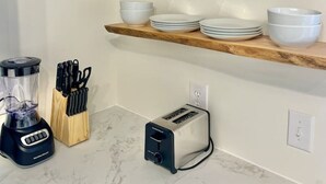 Une cuisine dotée de plans de travail en marbre, d’étagères en bois où sont posés des bols et des assiettes, d’un mixeur, d’un grille-pain et d’une plante.