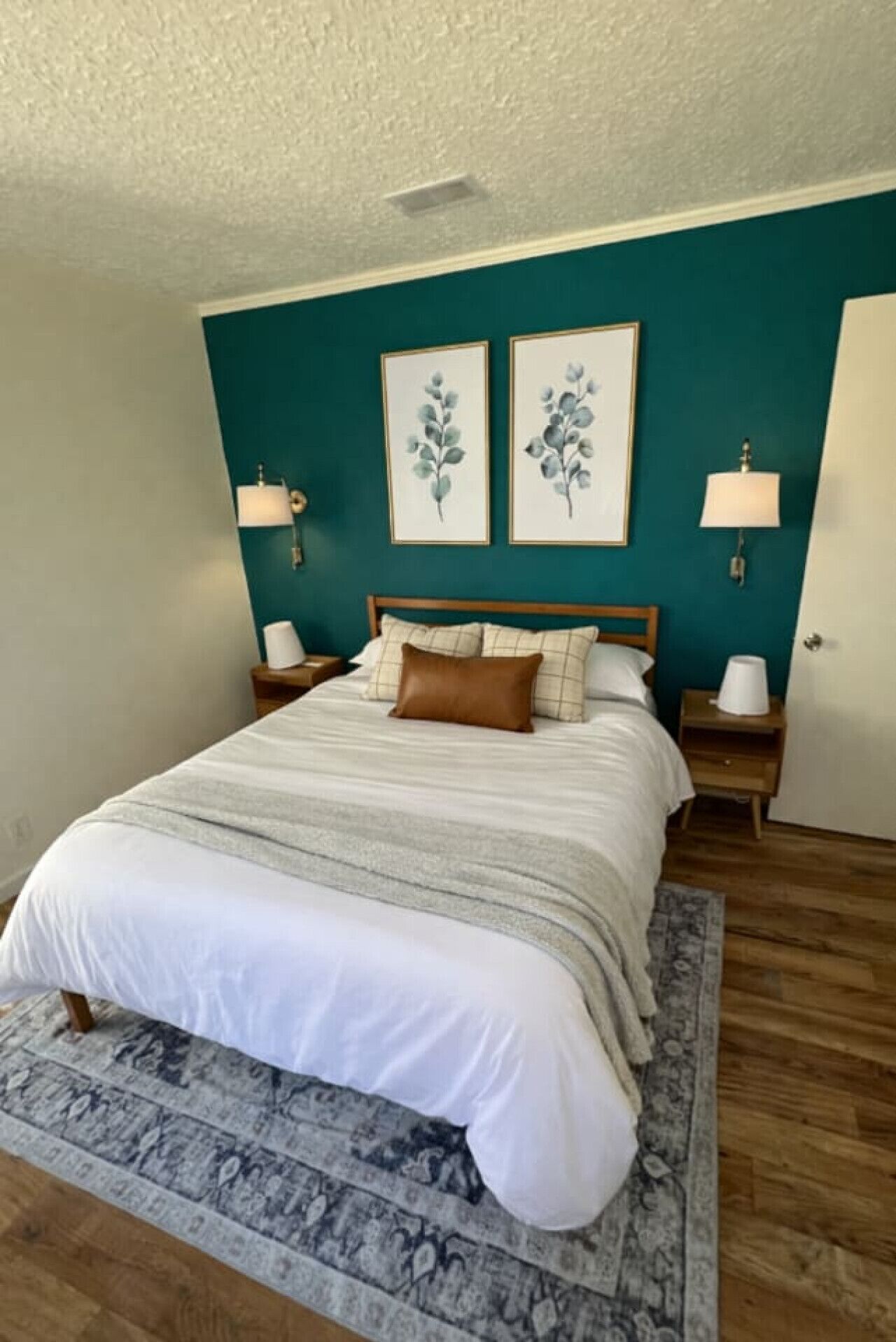 Ein Schlafzimmer mit einem Bett, zwei Nachttischen, einer Wand in Türkis und zwei gerahmten floralen Bildern.
